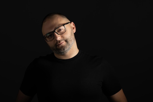 Un homme avec des lunettes regarde la caméra avec un regard attentif et agressif