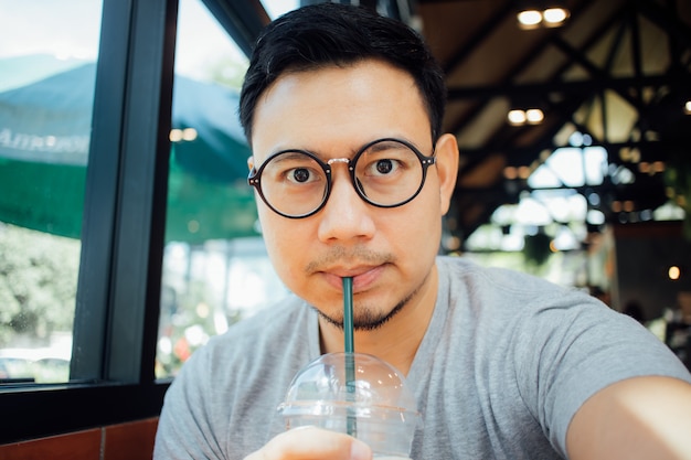 Homme avec des lunettes selfy boire du café au café.