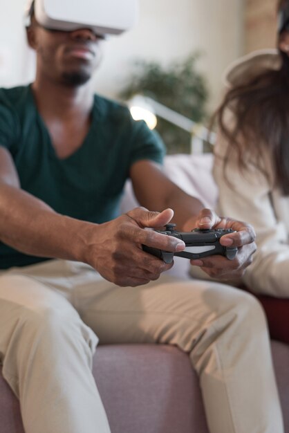 Homme à lunettes vr poussant les boutons du joystick et jouant à un jeu vidéo avec son ami sur le canapé