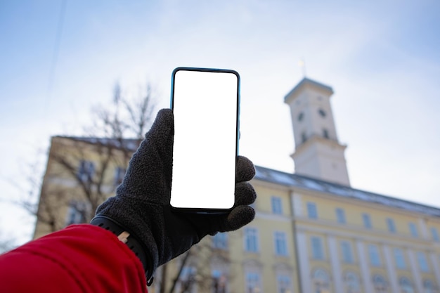 Homme main dans les gants tenant le téléphone avec l'hôtel de ville de lviv écran blanc sur fond