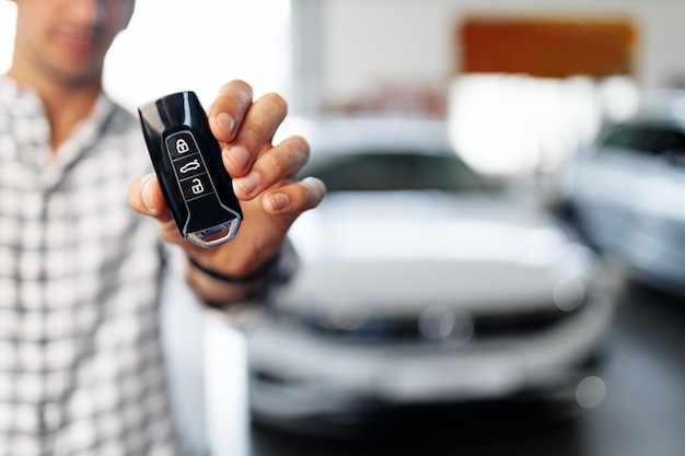 Homme main montrant les clés de voiture contre nouvelle voiture de luxe en concession