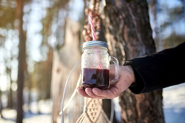 Homme main tenant un verre de vin chaud sur le d'une forêt d'hiver