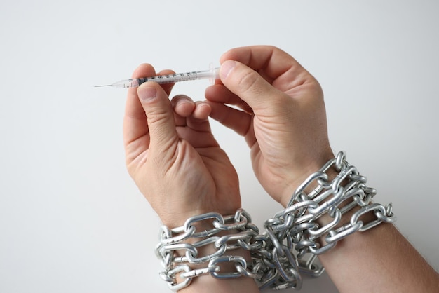 Homme avec les mains attachées avec une chaîne en métal tenant une seringue avec des médicaments en gros plan concept de toxicomanie