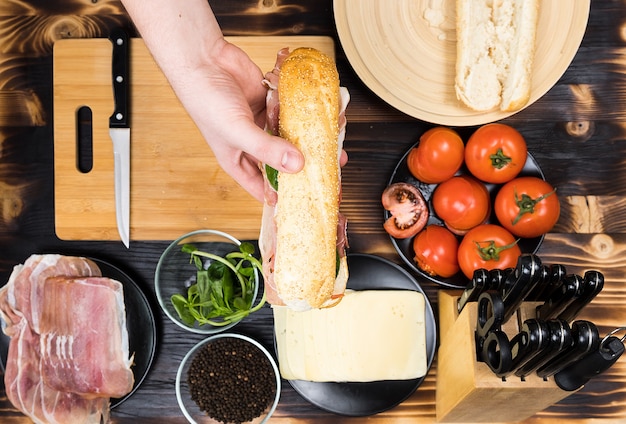 Un homme mains tient un sandwich fait maison sur une table de cuisine