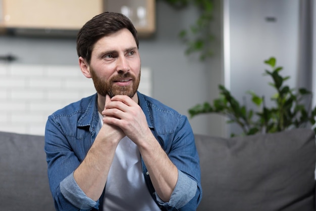 L'homme à la maison est assis sur le canapé au repos en détournant les yeux en souriant rêveur pensif