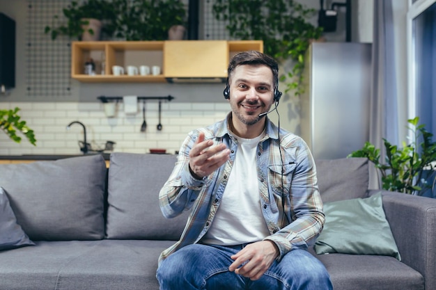 Un homme à la maison regarde la webcam et parle sur l'appel vidéo sourit et fait des gestes avec ses mains utilise un casque