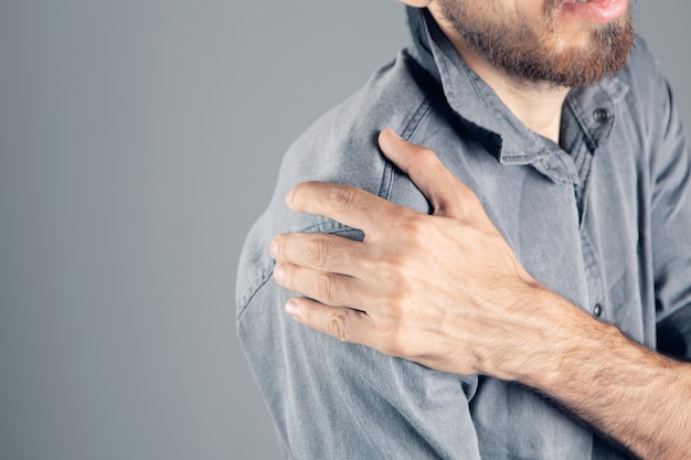 Un homme a mal à l'épaule sur fond gris