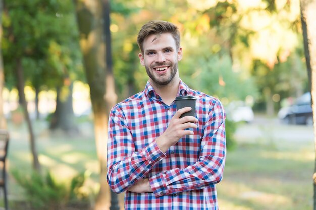 Homme mal rasé souriant buvant le café du matin en chemise à carreaux en plein air, inspiration.