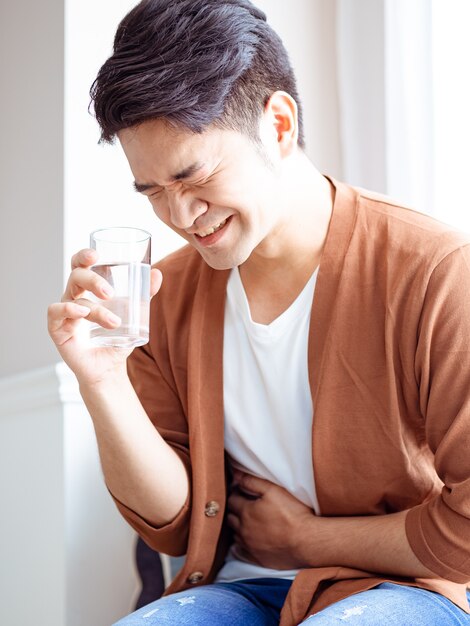 Un homme malade adulte en chemise avec un verre d'eau et tient sa main sur son ventre.