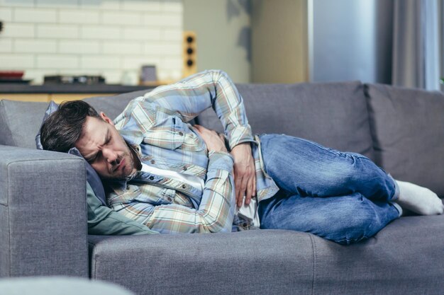 L'homme malade allongé sur le canapé à la maison a de fortes douleurs abdominales