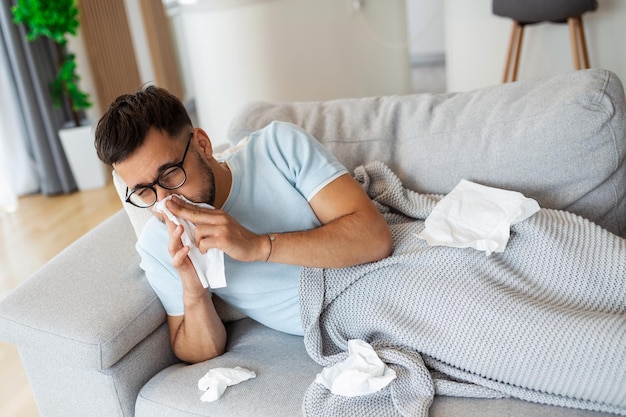 Homme malade allongé sur le canapé à la maison et se moucher Homme enveloppé dans un plaid allongé sur le canapé se sentant malade maladie à la maison