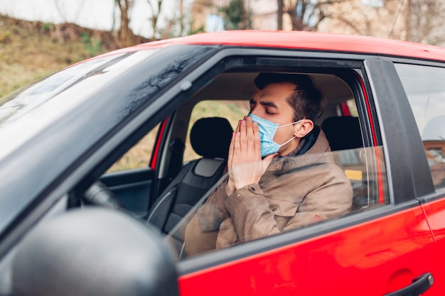 Homme malade assis dans une voiture portant un masque de protection contre la toux ayant un coronavirus grippal. Interdiction de conduire une voiture avec de la fièvre.
