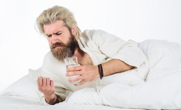 Homme malade au lit avec des pilules verre d'eau grippe saisonnière homme barbu couché dans son lit à la maison