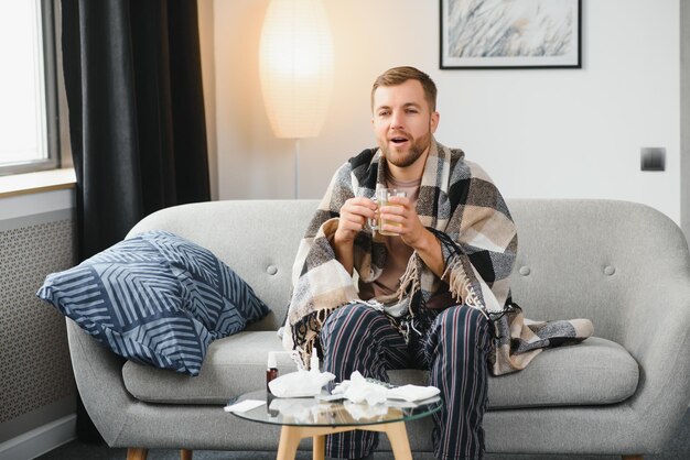 Un homme malade est assis à la maison sur un canapé gris avec une couverture Maladie protection coronavirus maladie grippe