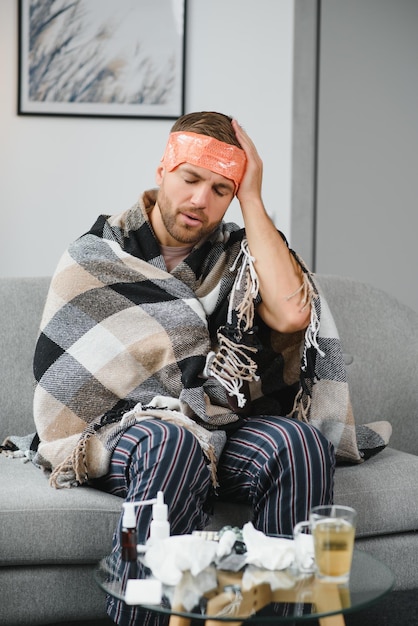 Un homme malade est assis à la maison sur un canapé gris avec une couverture Maladie protection coronavirus maladie grippe