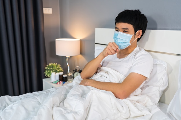 Homme malade en masque médical toussant et souffrant de maladie virale et de fièvre au lit, concept de pandémie de coronavirus.