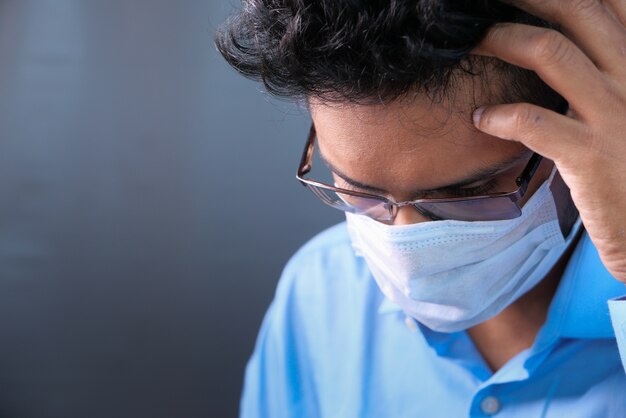 Un homme malade avec un masque protecteur dans le visage regardant vers le bas.