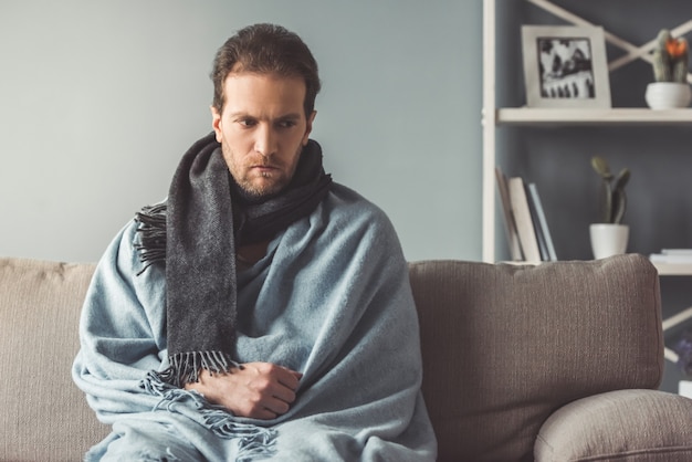 Un homme malade regarde tristement assis sur son canapé