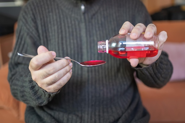 Homme malade versant du sirop dans une cuillère pour le prendre et soulager les symptômes de la maladie