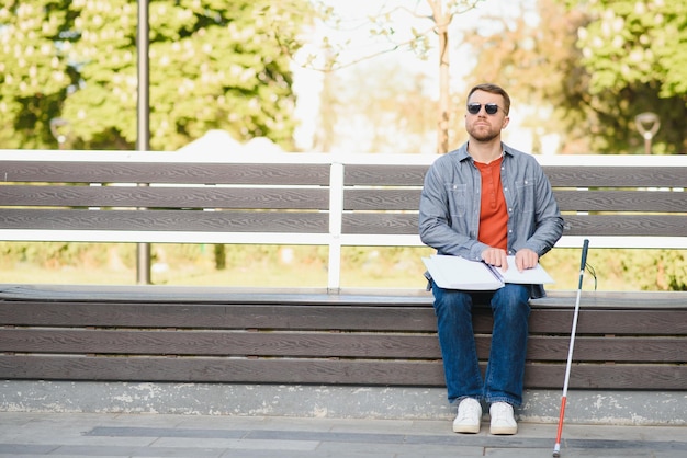 Homme malvoyant avec bâton de marche assis sur un banc dans le parc de la ville Espace de copie