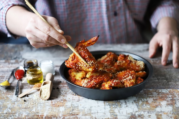 L'homme mange avec des ailes de poulet baguettes. Ailes de poulet à la chinoise avec graines de sésame.