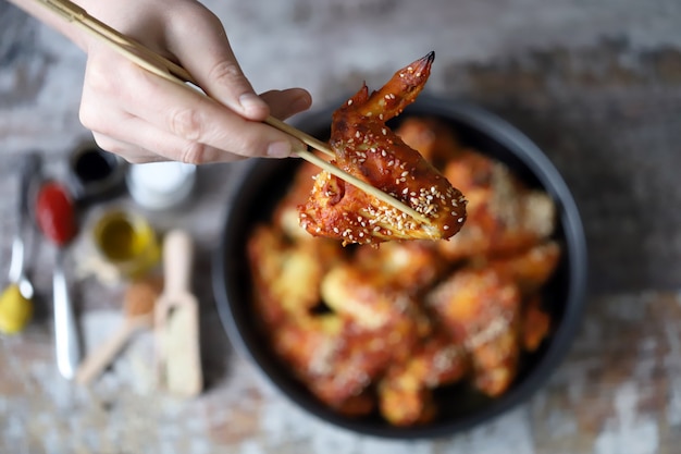 L'homme mange avec des ailes de poulet baguettes. Ailes de poulet à la chinoise avec graines de sésame.