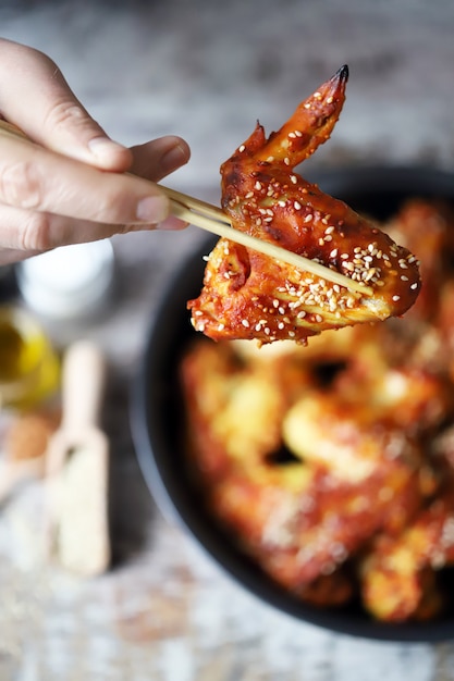 L'homme mange avec des ailes de poulet baguettes. Ailes de poulet à la chinoise avec graines de sésame.