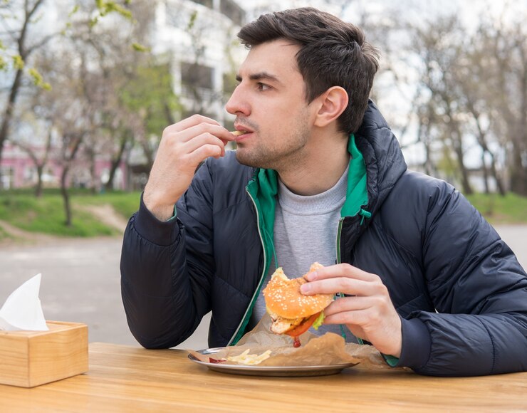 Photo l'homme mange des frites dans un snack-bar. un hamburger mordu se trouve sur la table.