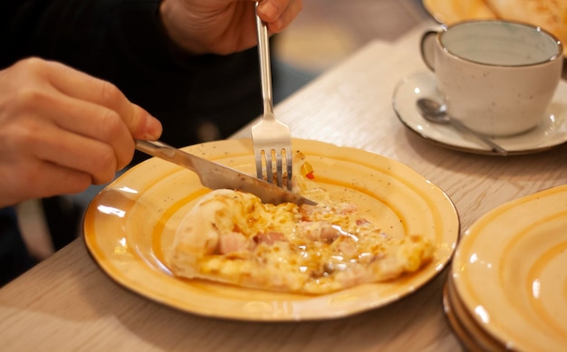 Un homme mange une pizza avec un couteau et une fourchette dans un restaurant