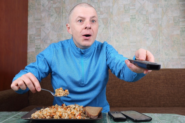 L'homme mange plov et regarde la télévision avec émotion