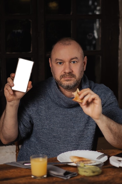 Un homme mange un sandwich et tient une maquette de téléphone dans ses mains Place pour le texte