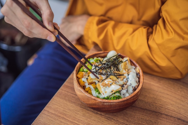 Homme mangeant un bol de poke bio cru avec du riz et des légumes gros plan sur la table vue de dessus