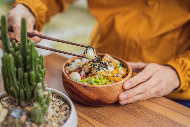 Homme mangeant un bol de poke bio cru avec du riz et des légumes gros plan sur la table vue de dessus