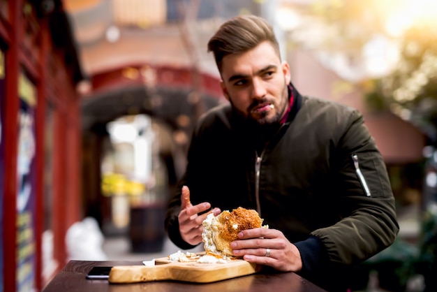 Homme mangeant un hamburger dans la rue. Délicieux burger.