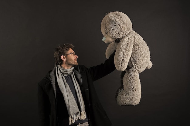 Homme en manteau et écharpe tenant un ours en peluche gris Homme barbu avec un gros jouet animal Cadeau et cadeau Mode et style Anniversaire ou anniversaire et célébration de vacances