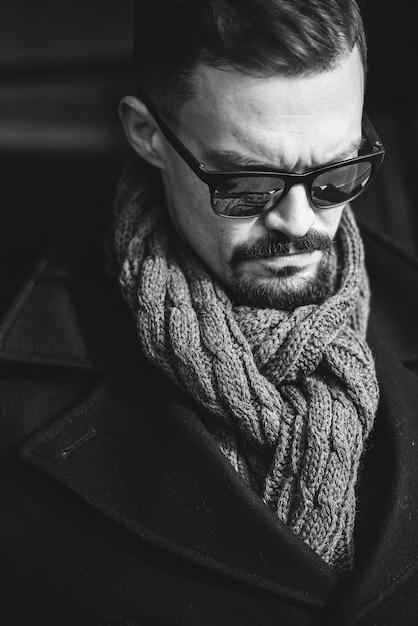 Un homme en manteau avec un foulard pose dans la rue pour faire de la publicité pour les vêtements pour hommes.