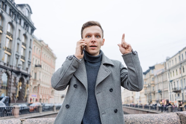 Homme en manteau gris et pull se dresse sur la rue de la ville Parle au téléphone Résout