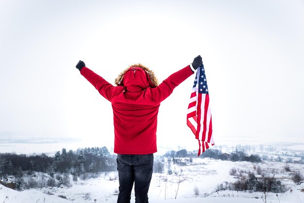 Homme en manteau d'hiver rouge tenant le drapeau américain à l'extérieur par temps de neige