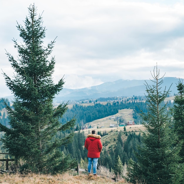 Homme en manteau rouge debout à la falaise avec vue magnifique sur les montagnes. endroit pour penser