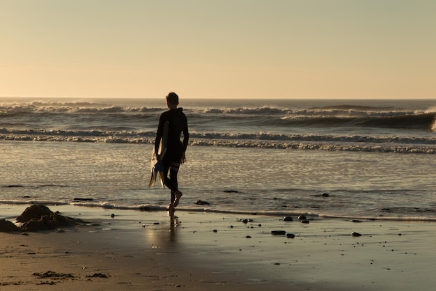 Homme marchant dans l'océan pour un surf avec un magnifique coucher de soleil