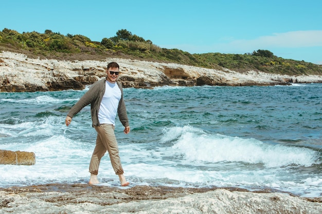 Homme marchant sur une plage rocheuse par temps venteux vacances d'été profiter de la vue sur la mer l'heure d'été