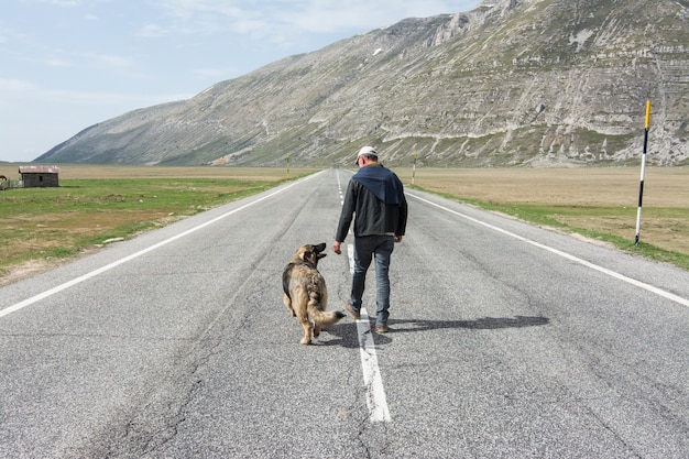 Homme marchant sur la route avec son chien dans les montagnes