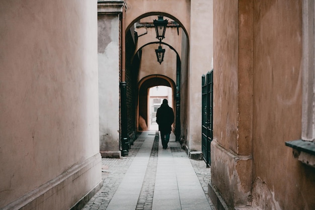 Un homme marchant à travers les arcades ombragées d'un bâtiment historique Quartier Vieille ville Architecture Histoire Ombre Homme marche seul dans une ruelle sombre Rue étroite