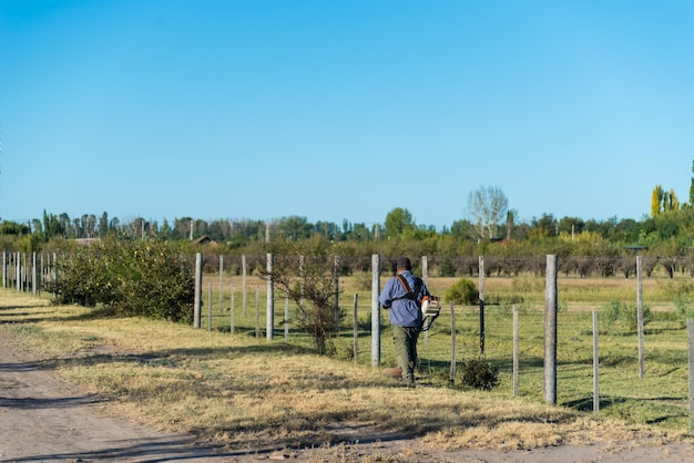 Un homme marche le long d'une clôture avec un sac bleu sur son épaule.