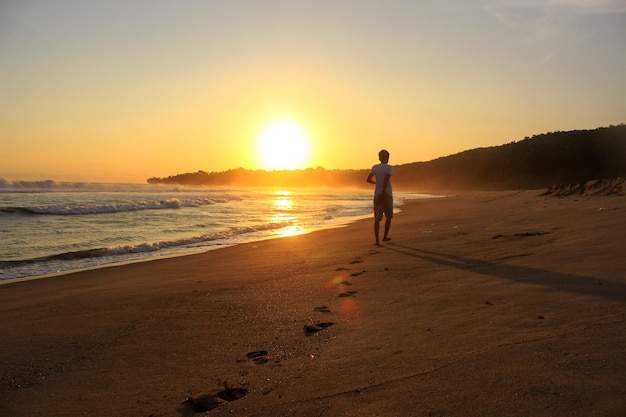 Un homme marche vers le soleil couchant en laissant des empreintes de pas dans le sable loin regarder de derrière