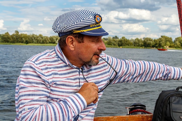 Homme marin dans une casquette sur un bateau sous voile contre le ciel et l'eau