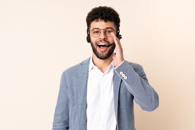 Homme marocain télévendeur travaillant avec un casque isolé sur beige avec surprise et expression faciale choquée