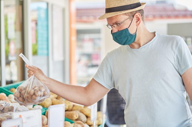 Un homme masqué achète des légumes sur un marché de fermiers de rue Concept de quarantaine du coronavirus Photo de haute qualité