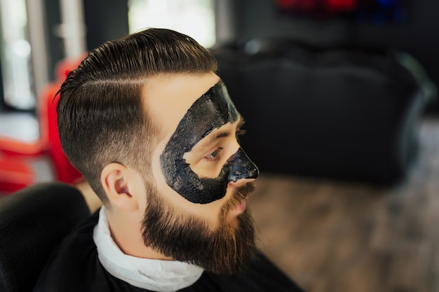 homme avec masque de charbon noir, soins de la peau concept, nettoyage des pores de l'acné.