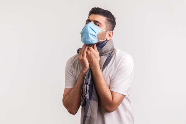Homme en masque et écharpe souffrant de maux de gorge, de toux et d'étouffement, présentant des symptômes de covid-19